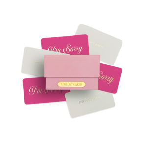 A collection of Apology Cards in pink and the packaging box on a transparent background, featuring various phrases including “I’m Sorry” printed in gold leaf.